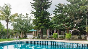 A swimming pool with a white fence, surrounded by trees and a building with columns. - Rancho Hotel El Carmen (Tlapacoyan)