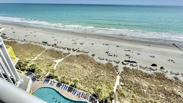 A beach view from a hotel balcony with a pool and lounge chairs.