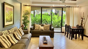A living room with a sofa, a coffee table, and a dining area with chairs and a table. - First floor Condo with large terrace - walking distance to the beach & town (JACO)