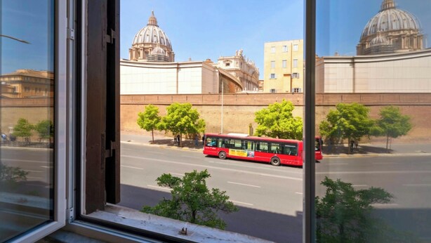 A red bus on a city street with large domed buildings in the background. - Luxury Designer Rome  — St. Peter Dome View (Roma)