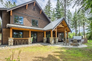 A modern log cabin with a covered patio, outdoor seating, and a grill area.