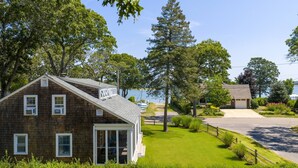 A two-story wooden house with a sloped roof, a covered porch, and a view of a lake. - Lovely Shelter Island cottage with panoramic bay views, secluded, screened... (Shelter Island)