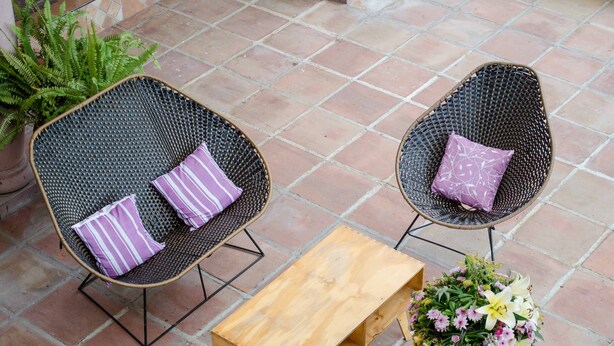Deux chaises en osier avec des coussins, une table en bois et une plante en pot ornée de fleurs.