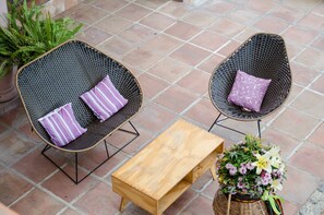 Two wicker chairs with cushions, a wooden table, and a potted plant with flowers. - Hotel Muñoz De Luna (Huajuapan)