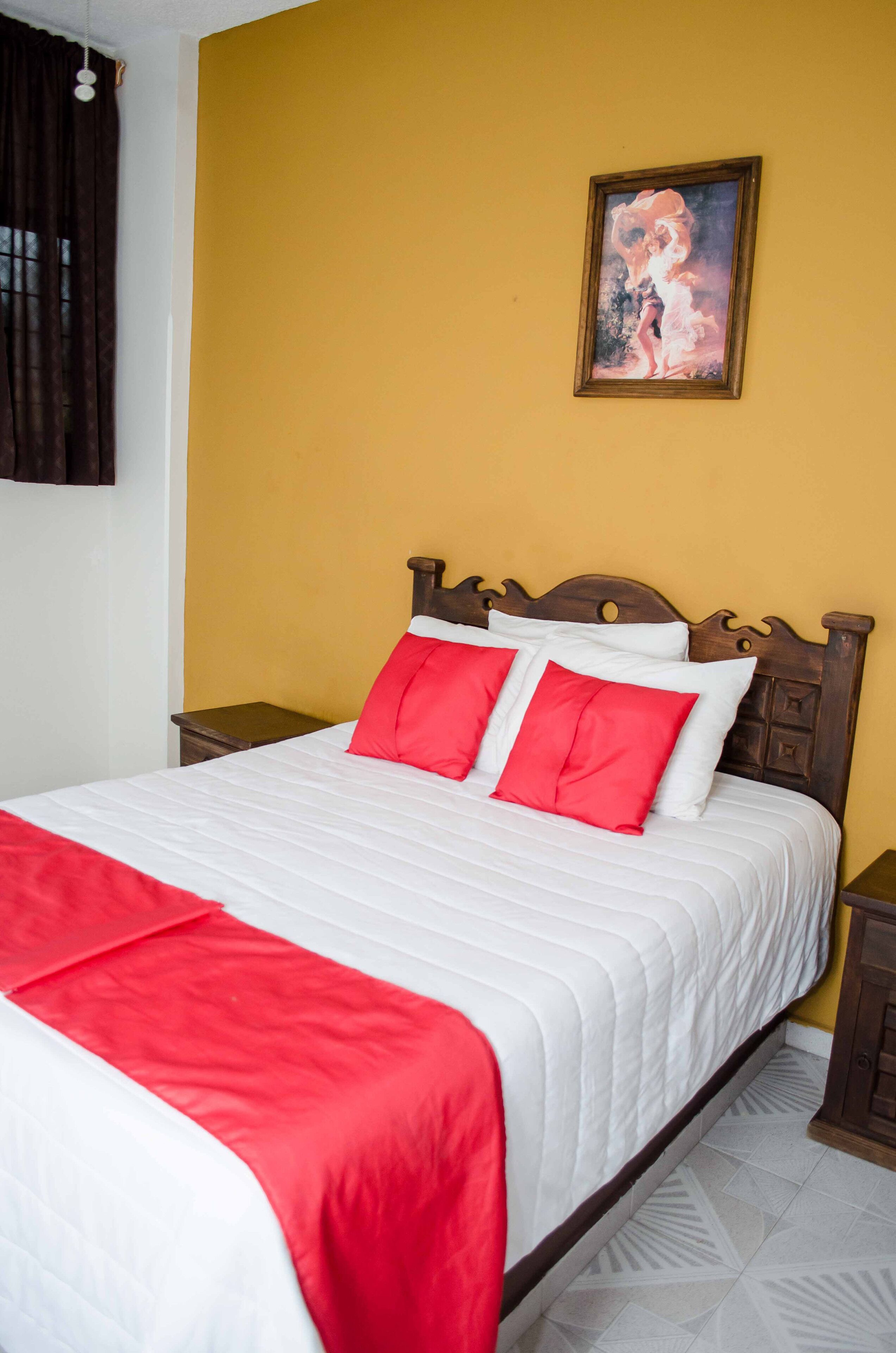A neatly made bed with white and red bedding, a wooden headboard, and a painting on the wall.
