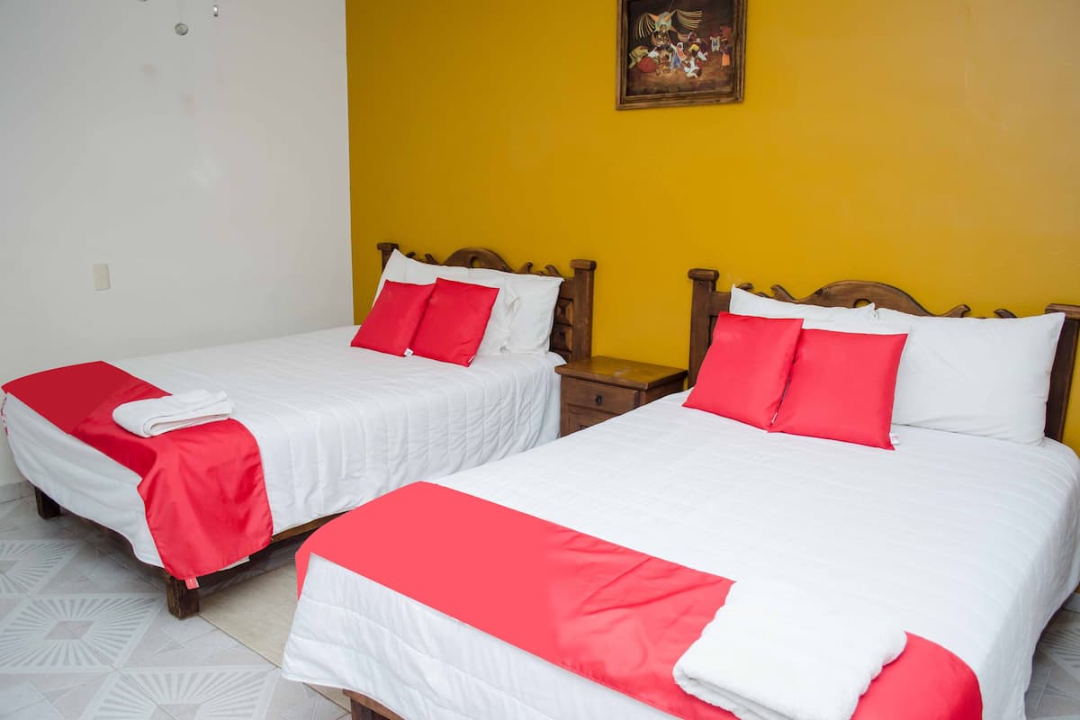 Dos camas individuales con ropa de cama roja y blanca, cabeceros de madera y una pared amarilla con un cuadro enmarcado.