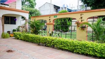 A courtyard with a tiled floor, a yellow wall with arched windows, and green hedges.