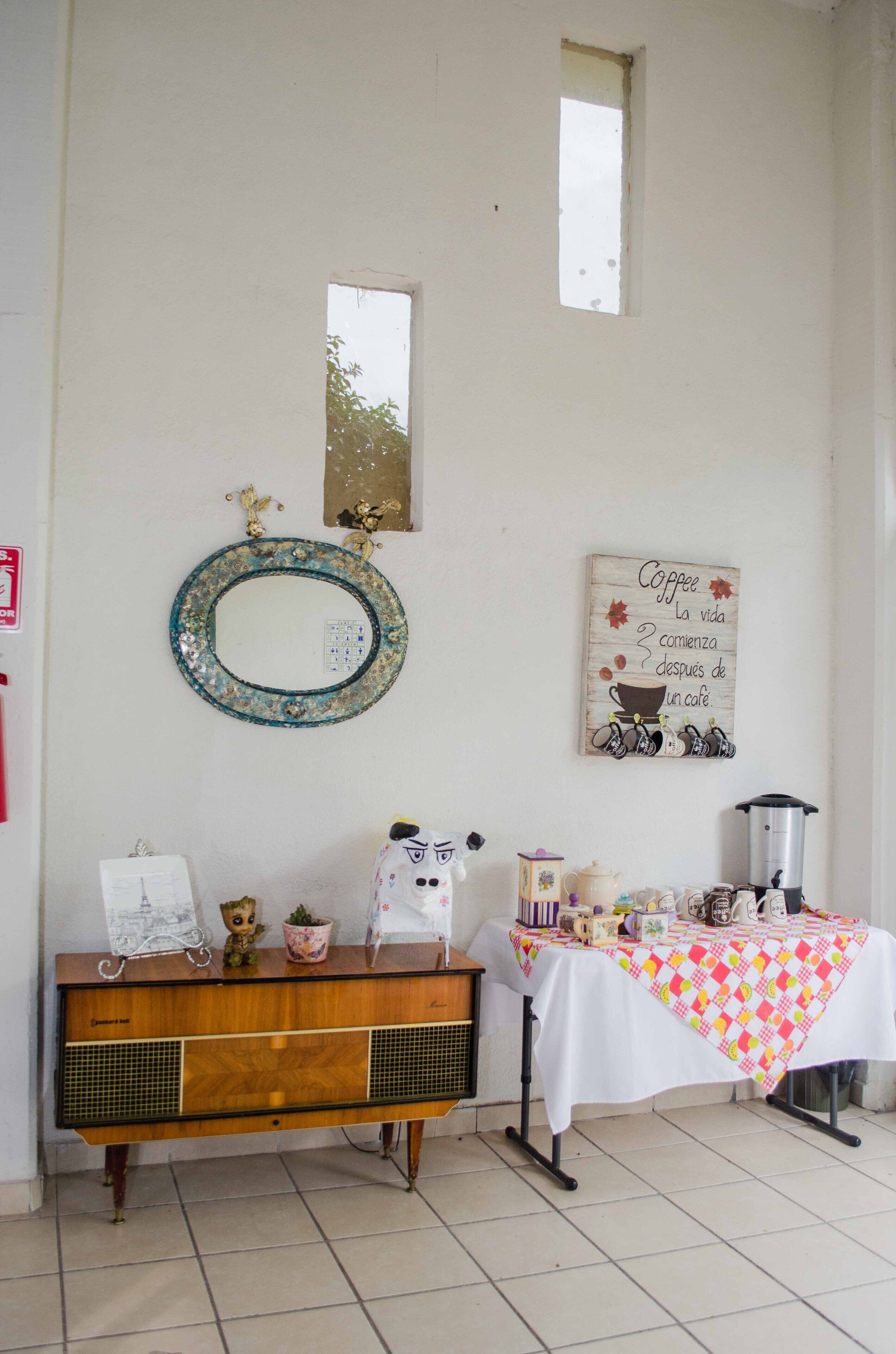 A room with a wooden console table, a mirror, a coffee-themed wall decoration, and a table with a checkered tablecloth.