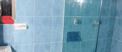 Un baño con azulejos azules, un inodoro blanco, una cabina de ducha con paredes de vidrio y un letrero azul que indica lavar las manos después de usar el baño.