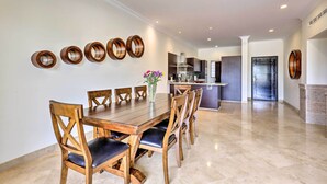 A dining area with a wooden table and chairs, a vase with flowers, and a kitchen in the background. - Walk to Beach: Modern Cabo Condo w/ Balcony! (Cabo San Lucas)