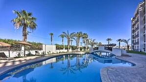 A clear blue pool surrounded by palm trees and modern buildings. - Walk to Beach: Modern Cabo Condo w/ Balcony! (Cabo San Lucas)