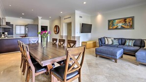 A modern living room with a dark-colored sofa, a dining table with wooden chairs, and a kitchen area in the background. - Walk to Beach: Modern Cabo Condo w/ Balcony! (Cabo San Lucas)