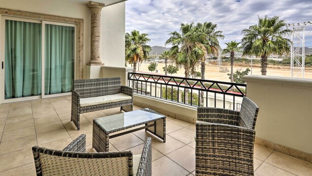 A balcony with wicker furniture, a glass door, and a view of palm trees and mountains. - Walk to Beach: Modern Cabo Condo w/ Balcony! (Cabo San Lucas)