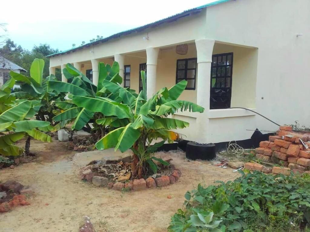 Un edificio con un porche cubierto, una palmera de plátano y una pared de ladrillo.