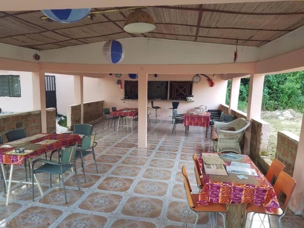 Un área de comedor al aire libre cubierta con varias mesas y sillas, una pantalla de televisión y un techo de paja.