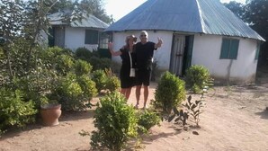 A rustic house with a corrugated metal roof, surrounded by small plants and a dirt ground. - Camping Sitaba Lodge (Janjanbureh)