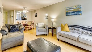 A living room with a grey sofa, a grey armchair, a black ottoman, a dining table with chairs, and a lamp. - Walk to Beach, Coligny Plaza | Hilton Head Villa (Hilton Head Island)