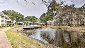 A serene courtyard with a fountain, surrounded by trees and a pathway leading to a building with balconies. - Walk to Beach, Coligny Plaza | Hilton Head Villa (Hilton Head Island)