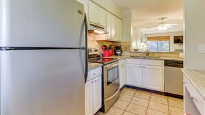 A kitchen with white cabinets, stainless steel appliances, a tiled floor, and a ceiling fan. - Walk to Beach, Coligny Plaza | Hilton Head Villa (Hilton Head Island)