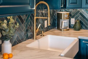 A kitchen with a modern design, featuring a gold faucet, a coffee maker, and a white sink.