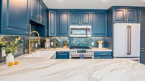 A kitchen with blue cabinets, a white refrigerator, a stainless steel oven, and a marble countertop.