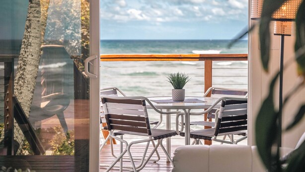A balcony with a view of the ocean, featuring a table and chairs, a potted plant, and a railing.