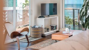 A living room with a TV on a white stand, a sofa, a coffee table, and a view of the ocean.