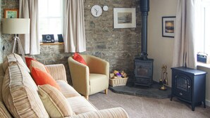 A cozy living room with a stone wall, a sofa, a chair, a lamp, a clock, a fireplace, and a window with curtains. - The Coach House - UK30813 (Thornthwaite, near Keswick)