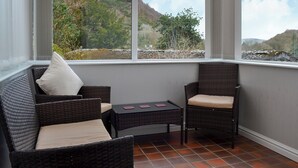 A sunroom with wicker furniture, a small table, and a view of a mountainous landscape. - The Coach House - UK30813 (Thornthwaite, near Keswick)