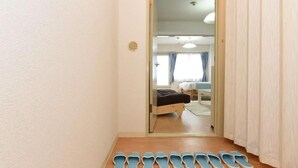 A hallway with a row of slippers on the floor, leading to a room with a bed and a desk. - Kentaku29 BLD. 72 (Sapporo)