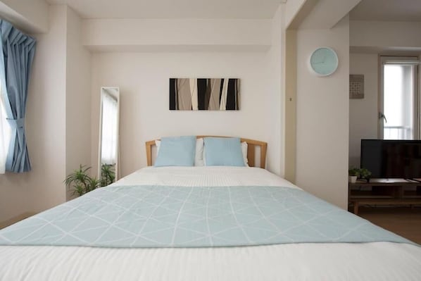 A bedroom with a bed, a mirror, a clock, and a TV.
