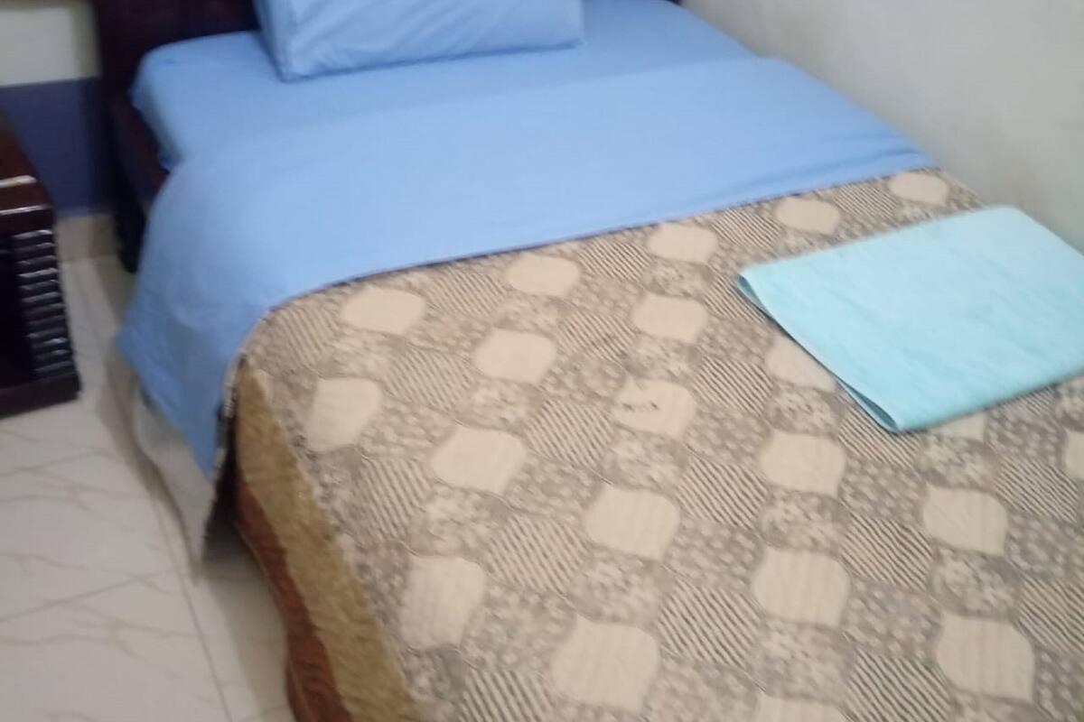 A single bed with a patterned bedspread and a blue pillow.