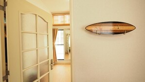 A hallway with a frosted glass door, a wooden surfboard mounted on the wall, and a view into another room. - Opus 802 (Sapporo)
