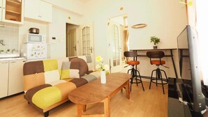 A compact living space with a sofa, a dining table, a kitchen area with a microwave, and a TV. - Opus 802 (Sapporo)
