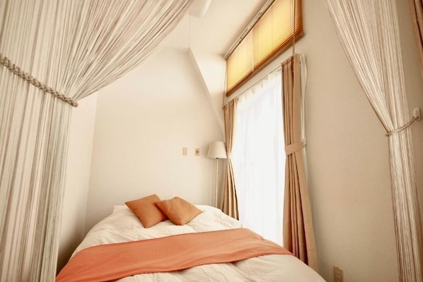A bedroom with a bed, curtains, a lamp, and a window.