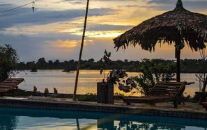 A poolside area with a thatched umbrella, lounge chairs, and a view of a body of water during sunset. - Elizabeth Village and Resort (Buchanan)