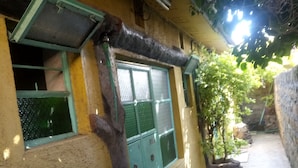 A narrow outdoor corridor with a yellow wall, a green door, and a window with a metal grill. - Venus lodge Kikopeye (Gilgil)