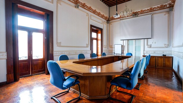 Una sala de conferencias con una gran mesa de madera, sillas azules y una pizarra.
