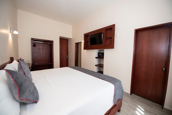 A hotel room with a large bed, wooden doors, a mounted TV, and a small shelf.