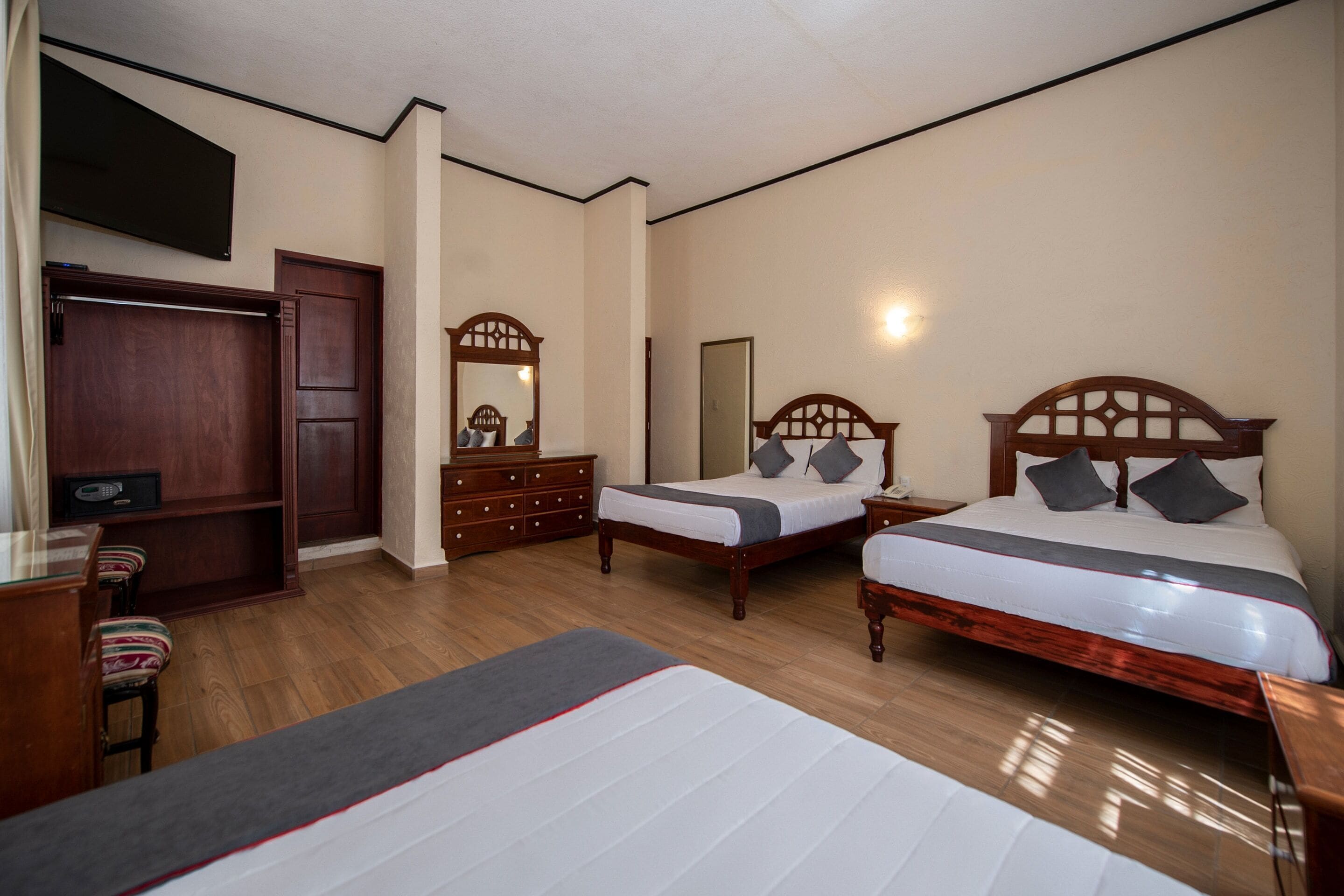 Una habitación de hotel con dos camas de madera, un tocador de madera, un espejo, un televisor y un armario de madera.