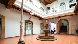 Ein geräumiger Innenhof mit einer zentralen Fontäne, eine hohe Decke mit Holzbalken und ein Balkon mit aufwendigen Geländern.