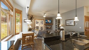 A spacious kitchen with a large island, wooden cabinetry, and a stone fireplace. - Beautiful mountain views from this immaculate 3 bedroom ski and summer condo (Whitefish)