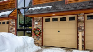 A two-story house with a garage door, stone facade, and a wreath on the door. - Beautiful mountain views from this immaculate 3 bedroom ski and summer condo (Whitefish)