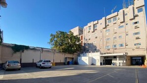 A parking lot with two cars, a building with multiple windows and balconies, and a tree in the background. - Hotel Impala de Tampico (Tampico)