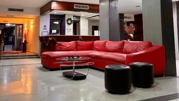 A modern lobby with a red sectional sofa, a small round table, and two black stools. - Hotel Impala de Tampico (Tampico)
