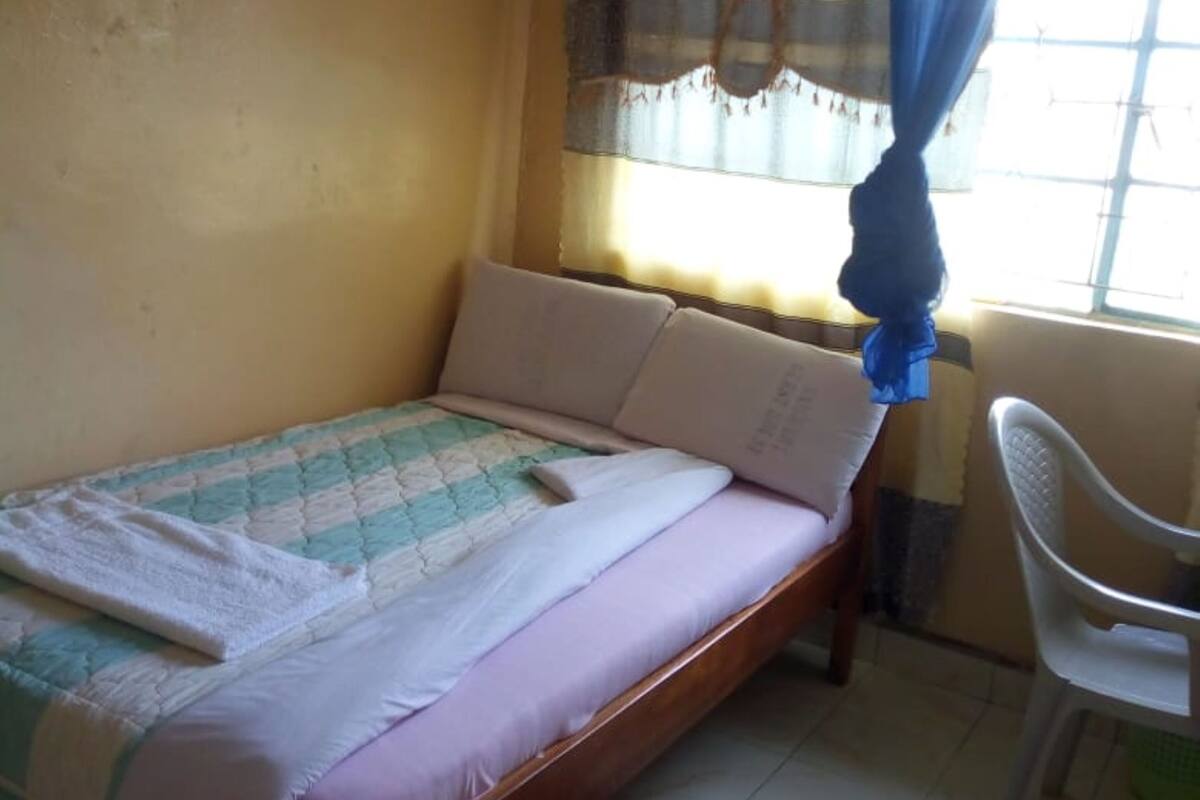 A single bed with a quilt, a chair, and a mosquito net.