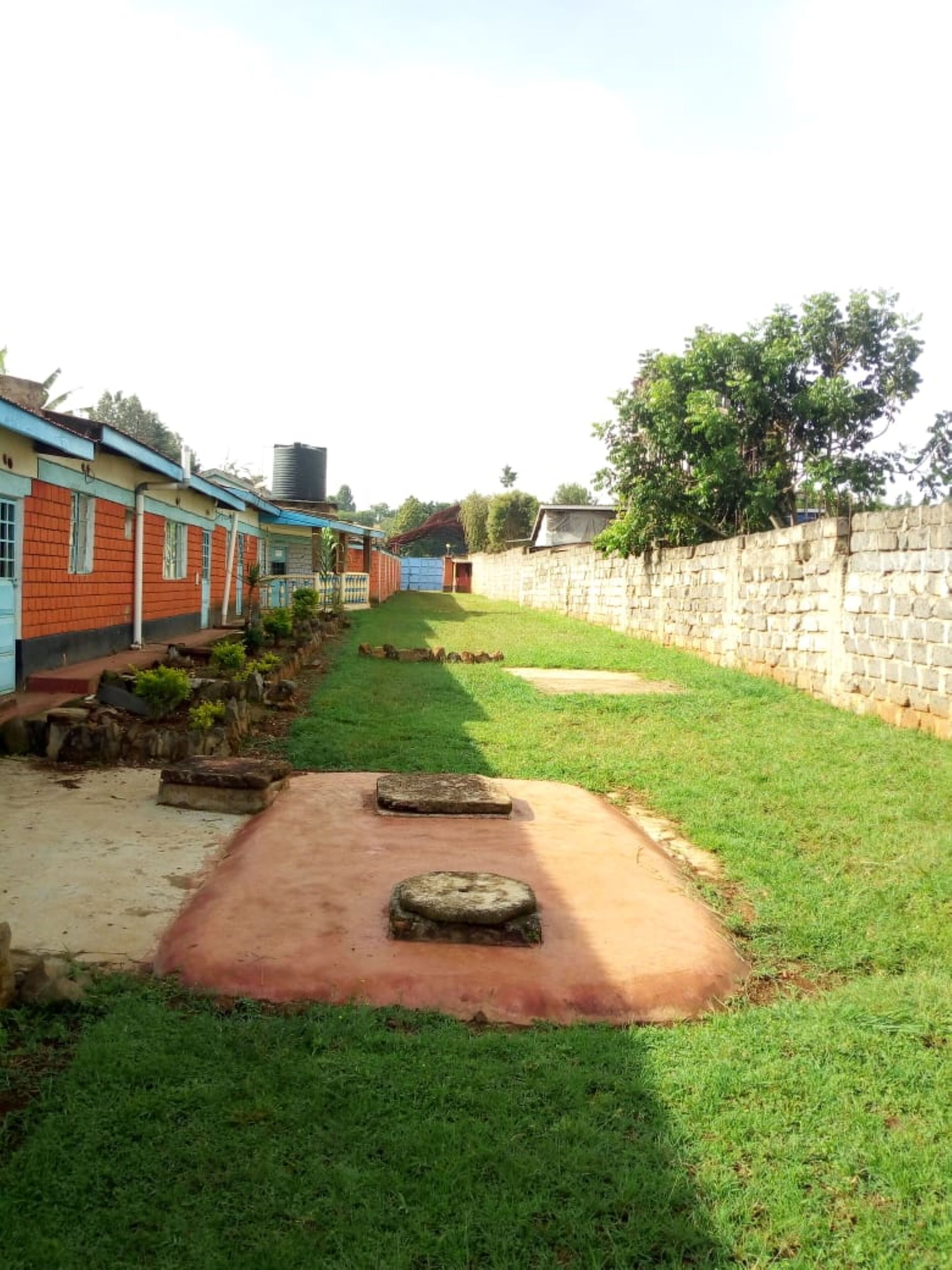 A narrow pathway leading to a building with a stone wall on one side and a row of houses on the other.