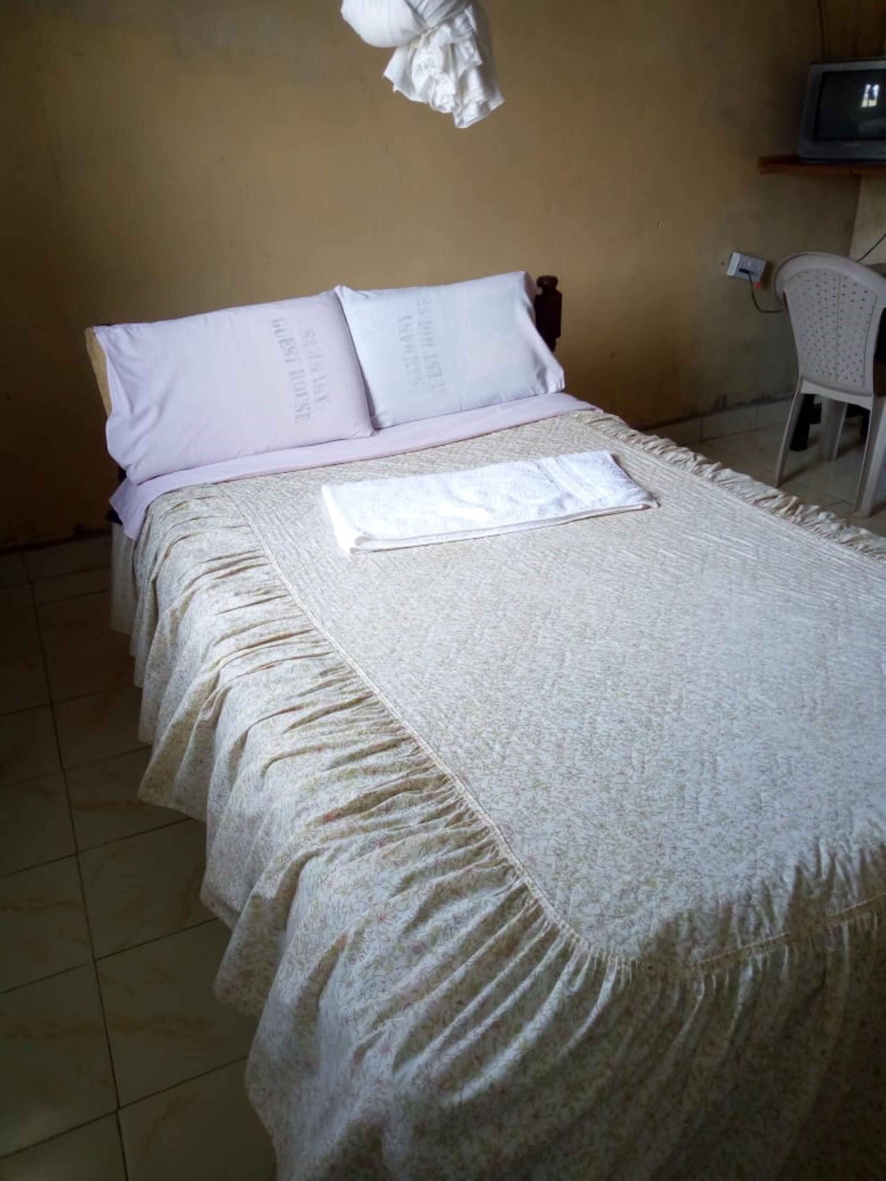 A bed with a patterned bedspread and pillows, a chair, and a television on a stand.