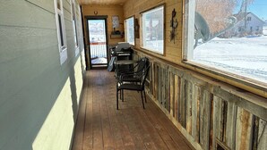 A covered corridor with wooden floors and walls, a grill, and a view of a snowy landscape. - Beautiful Bear Lake House, with big grassy yard, 4 mins to North Beach. (St Charles)