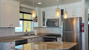 A modern kitchen with white cabinets, granite countertops, stainless steel appliances, and a central island with stools. - Beautiful Bear Lake House, with big grassy yard, 4 mins to North Beach. (St Charles)